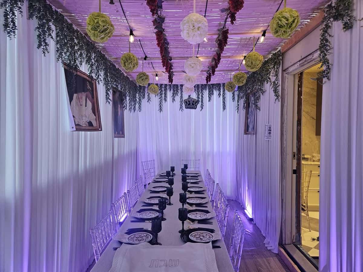 A finished sukkah prepared with schach, greenery, lighting and a set table