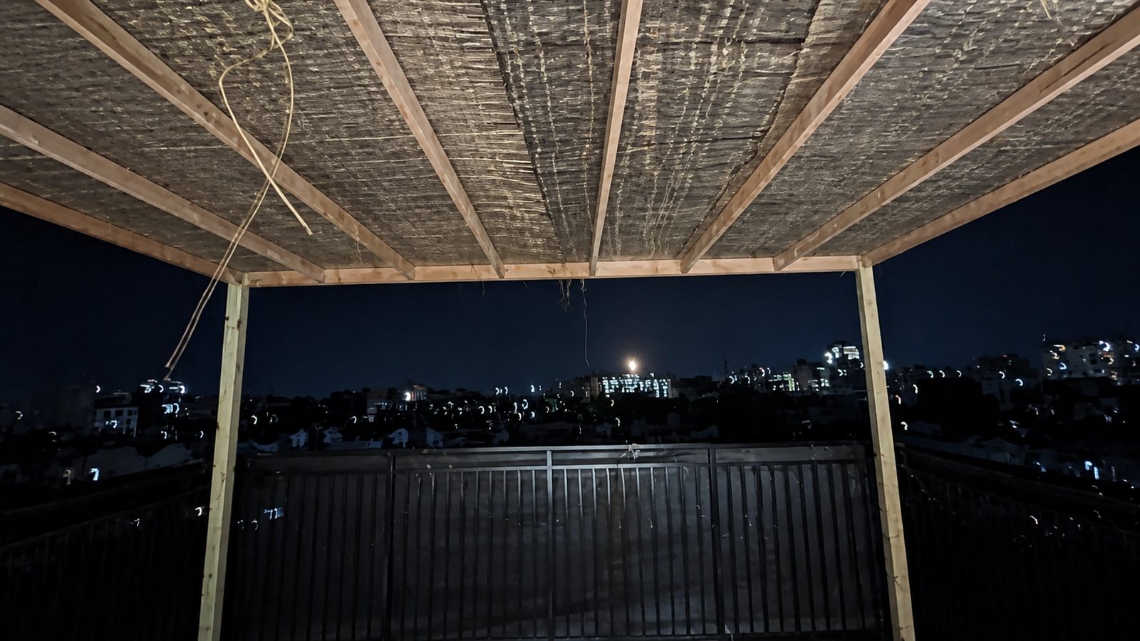 Interior view beneath a light wood pergola with a woven roof on a rooftop terrace